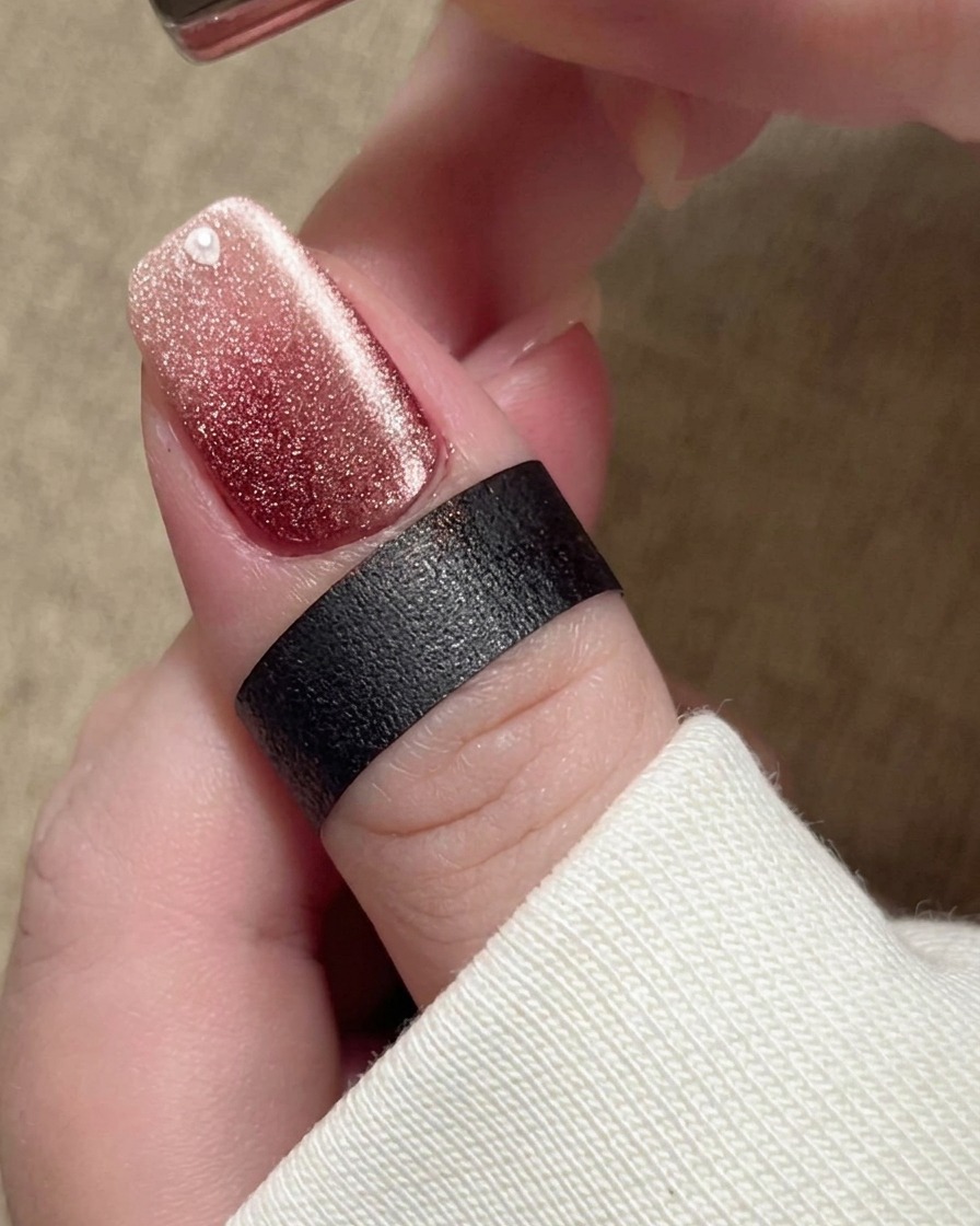 爪の近くに磁石を近づけ、ベージュのポリッシュ内の金属粒子を明るく幅の広いシマーバンドへと移動させている様子。