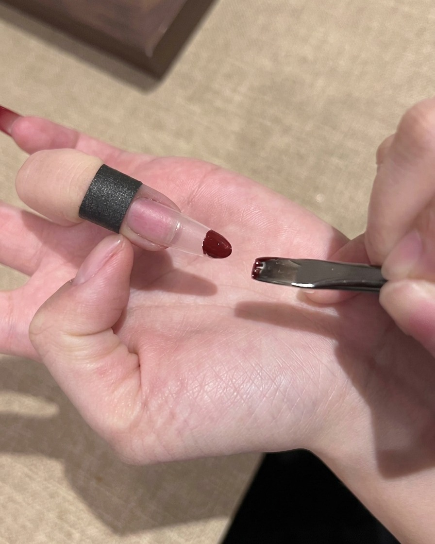 小さなメイクスポンジを使用して、クリアネイルチップの先端に赤いジェルポリッシュをポンポンと叩き込んでブレンドしている手元。