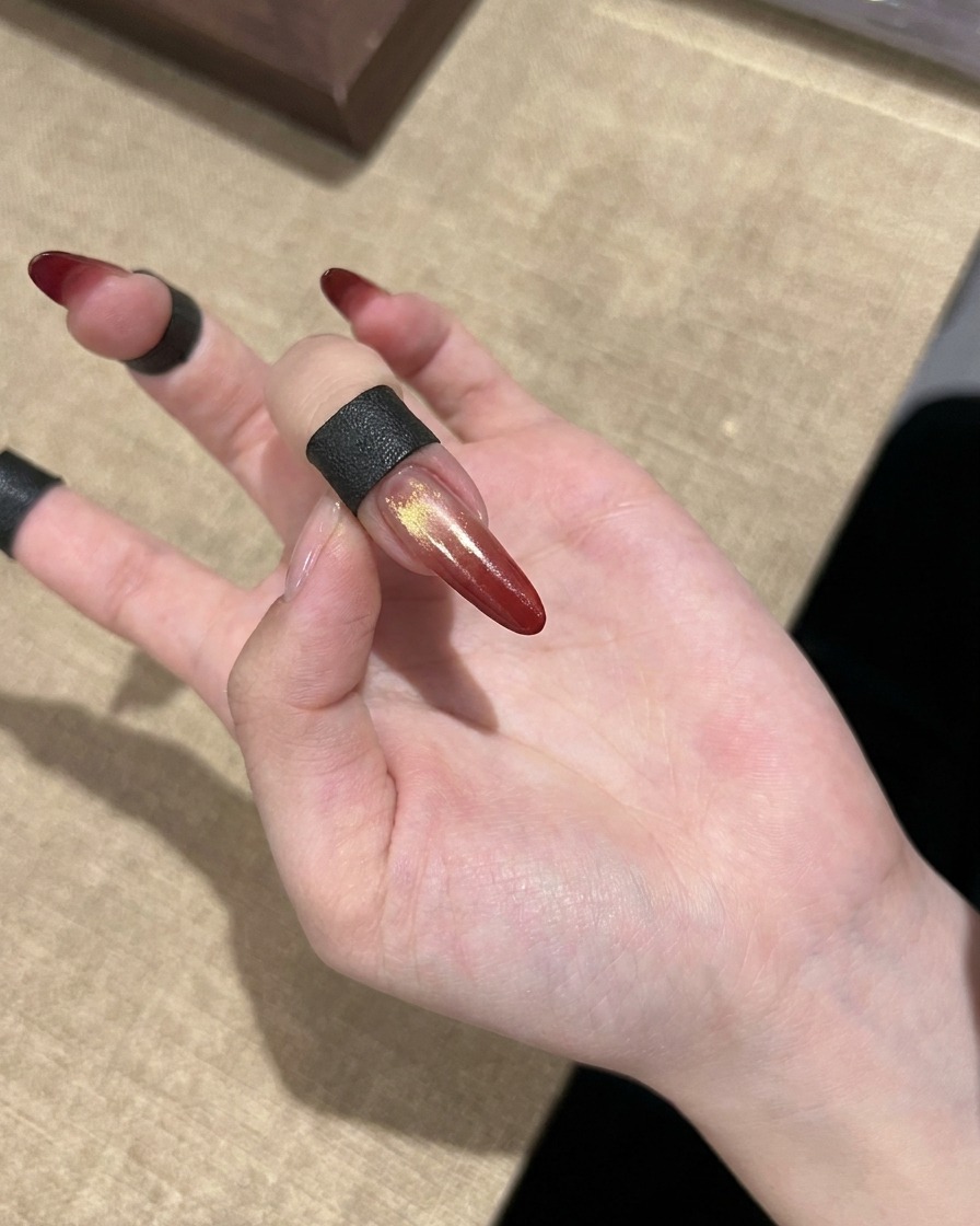 ゴールドのアクセントが入った、完成したレッドグラデーションのキャッツアイネイルが手元に示されている様子。