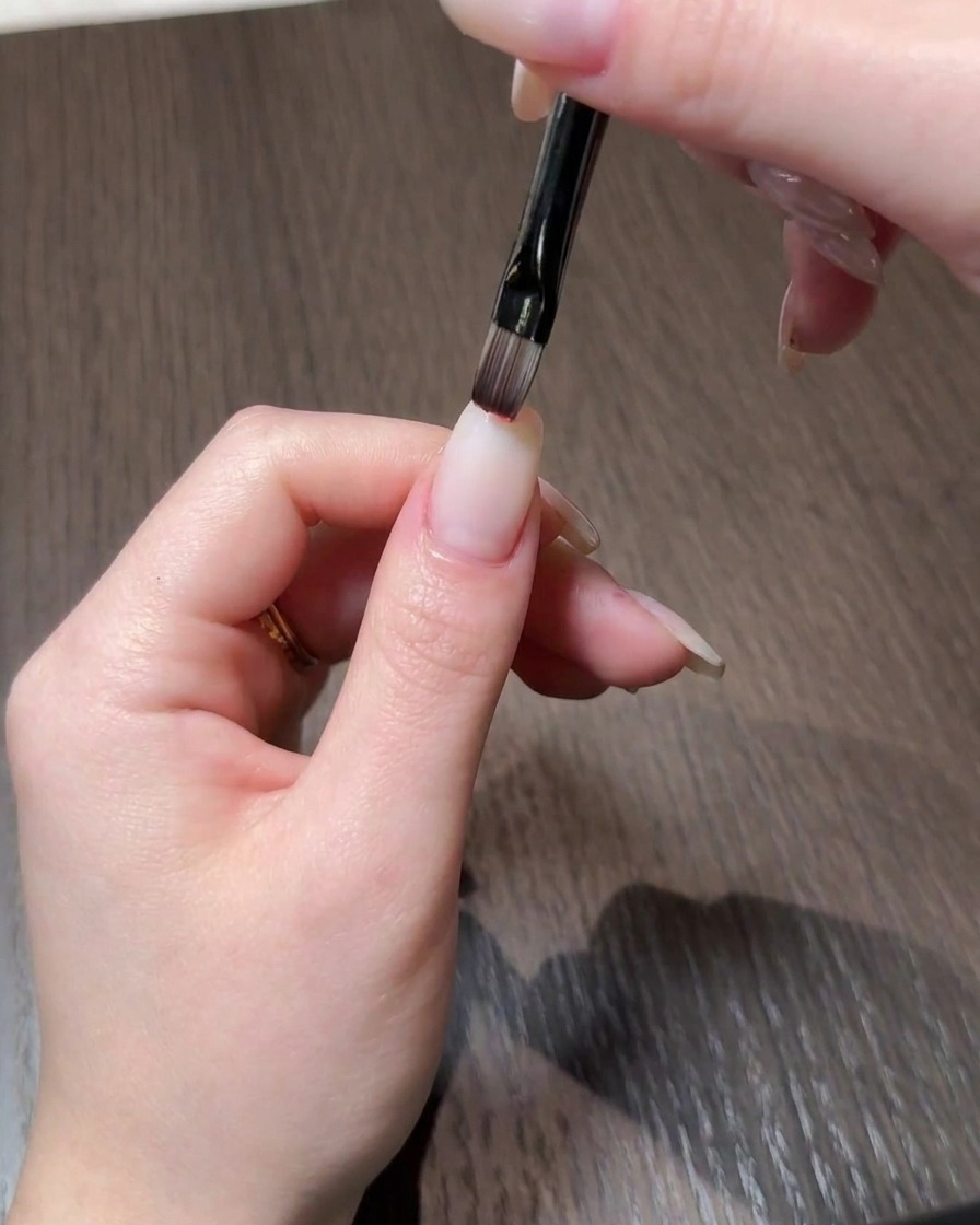 細いブラシを使用して、自爪風のネイルの先端に赤のジェルポリッシュを塗布している手元のクローズアップ。