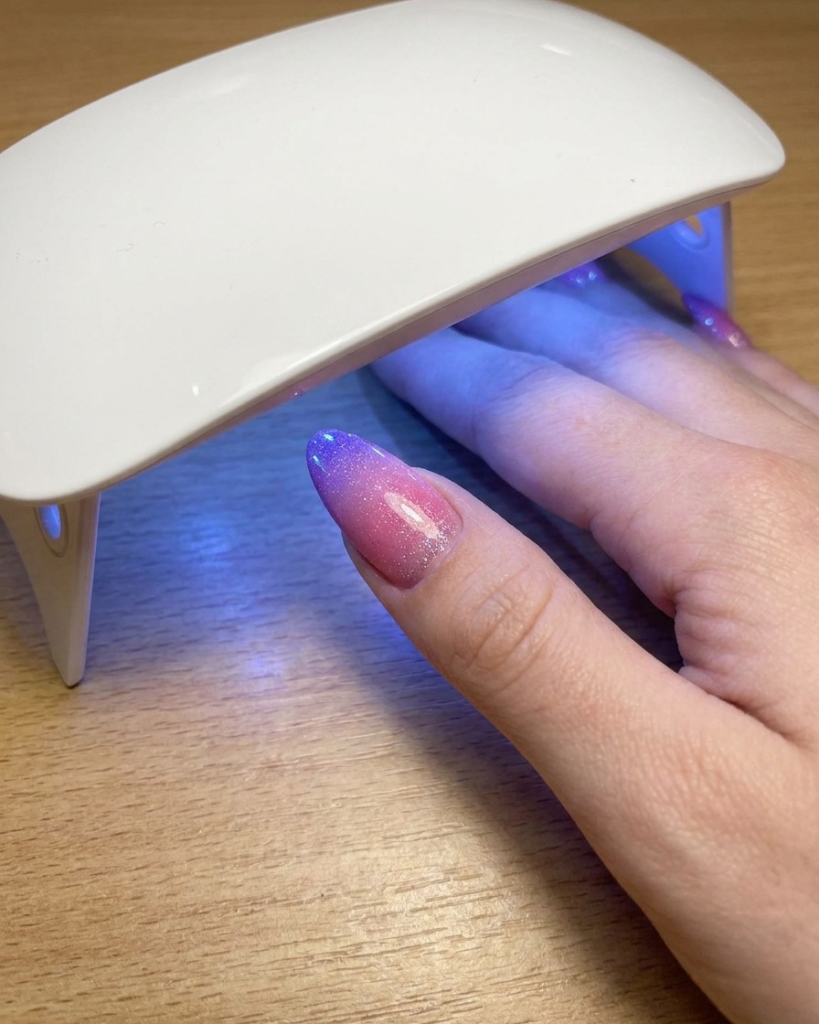 ポータブルなUVランプの下で、キャッツアイジェルポリッシュの最終層を硬化させながら休止している親指。
