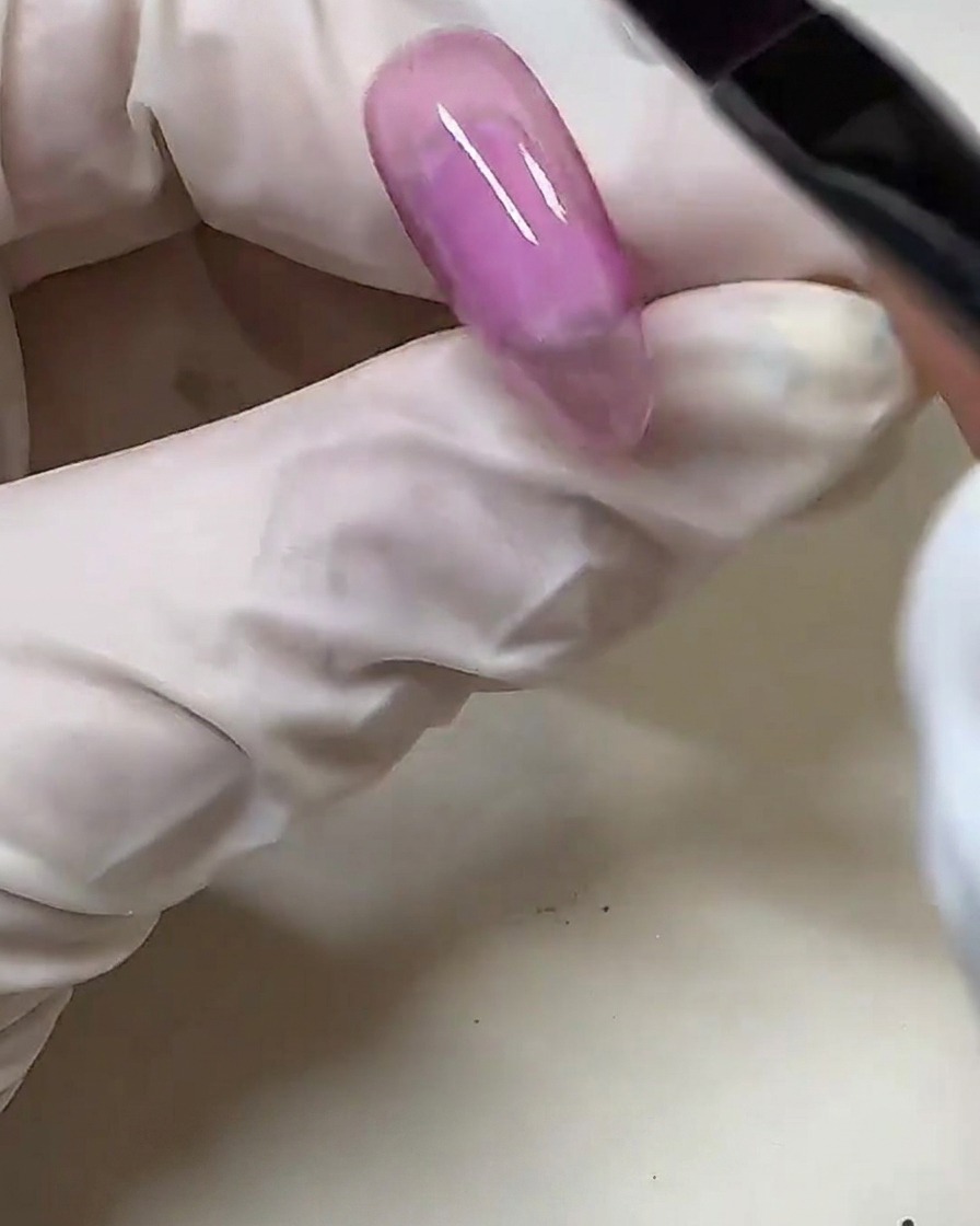 クリアなネイルチップにジェルブラシを使ってシアーなピンクジェルを塗っている手元。