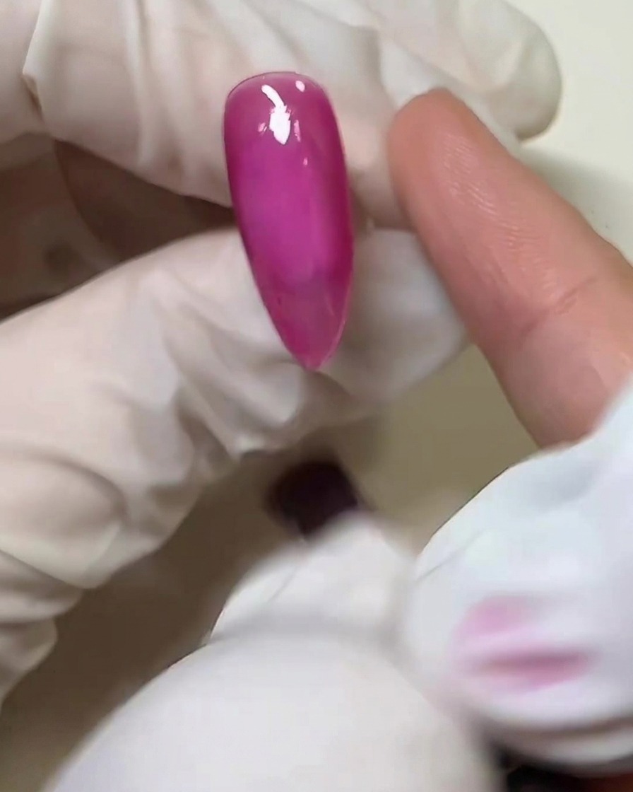 硬化したピンクのネイル表面に、指で透明なソリッドジェル(グミジェル)を薄く塗っているアップ画像。