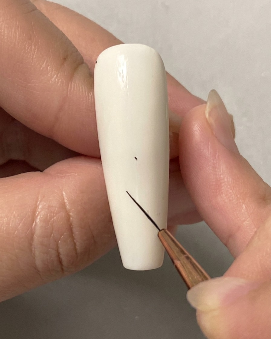 ソリッドな白いネイルの上に、極細ライナーブラシを使って小さなガイドドットを配置している手。