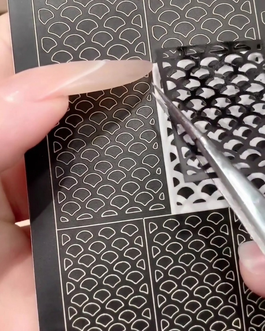 再利用性を示すために、ピンセットで黒いネイルアート用ステッカーの使用済みシートをめくっているところ。