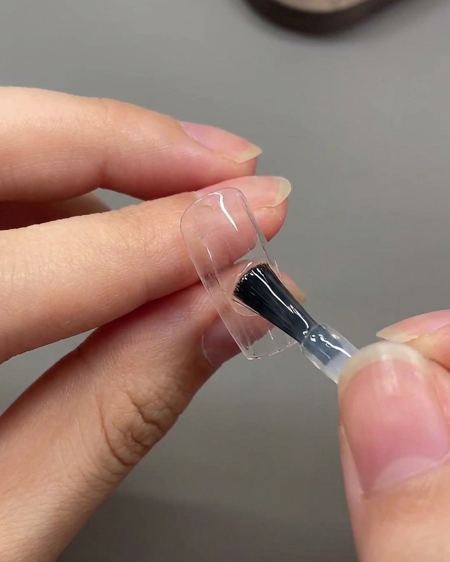 ブラシを使って爪の表面全体にマットトップコートの層を塗布している様子。