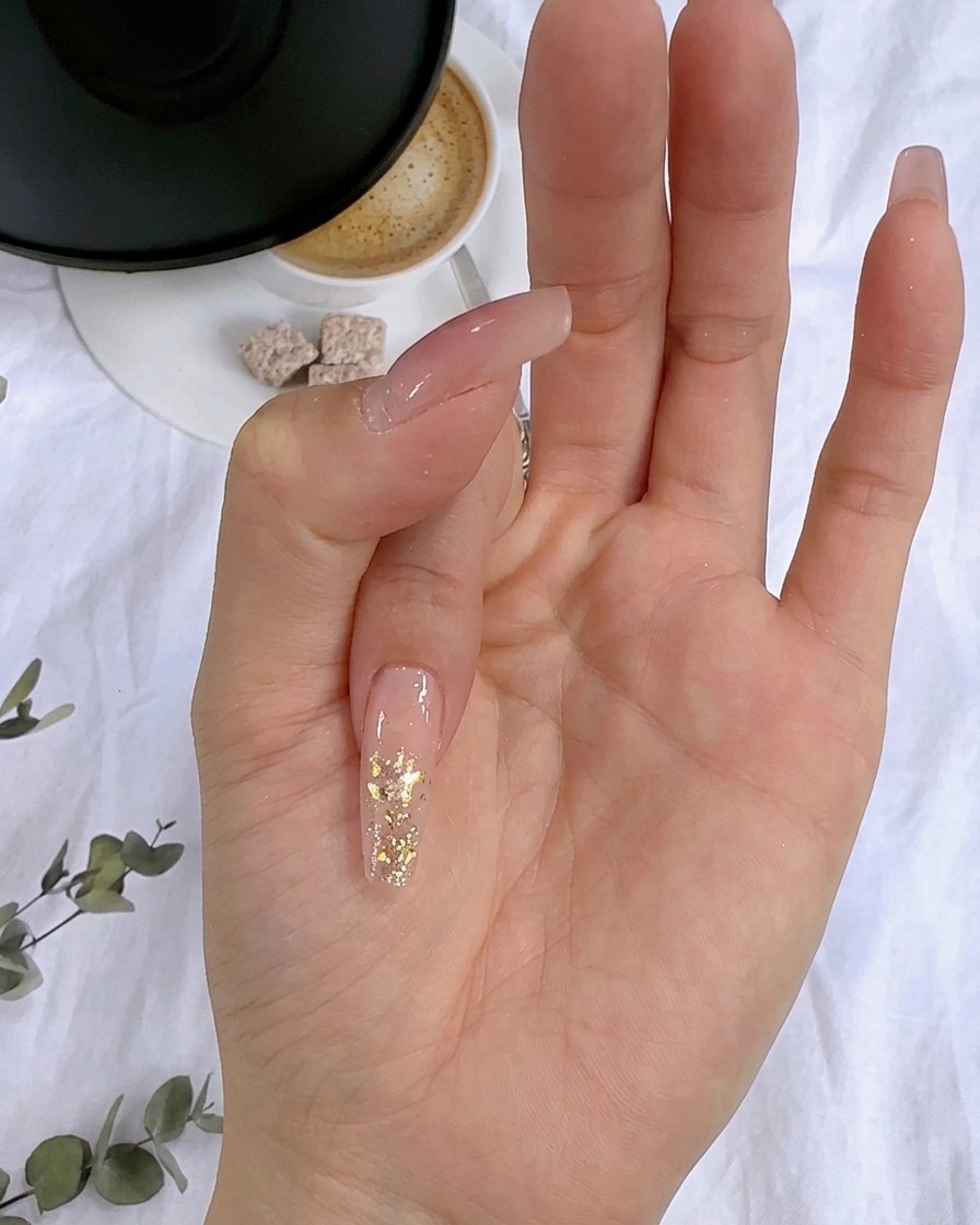 爪の上の硬化していないラメの層に、金箔を丁寧に押し当てているアップ画像。
