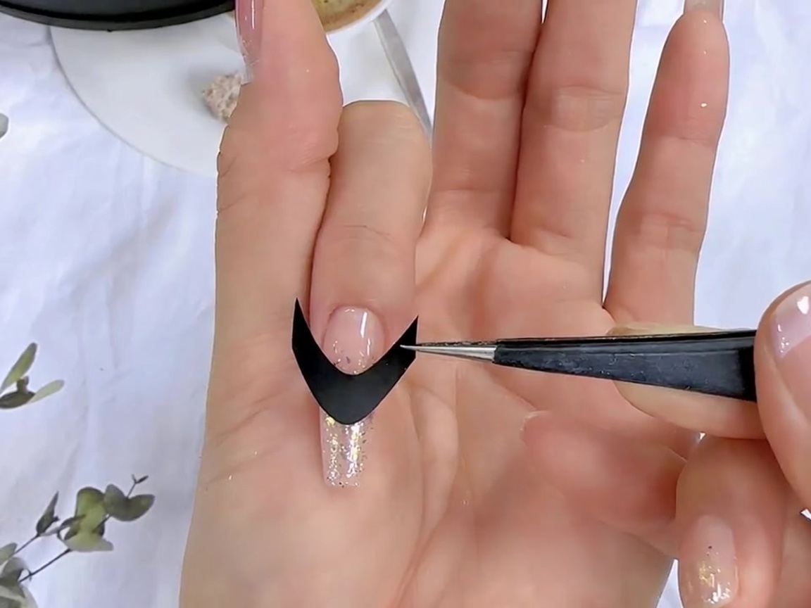 ピンセットを使って、準備が整った爪に黒いフレンチガイドシールを配置している様子。