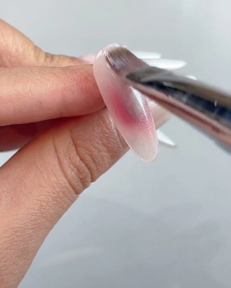 ネイルブラシで、下準備をしたネイルの表面全体にクリアなキャッツアイジェルの層を塗っている様子。