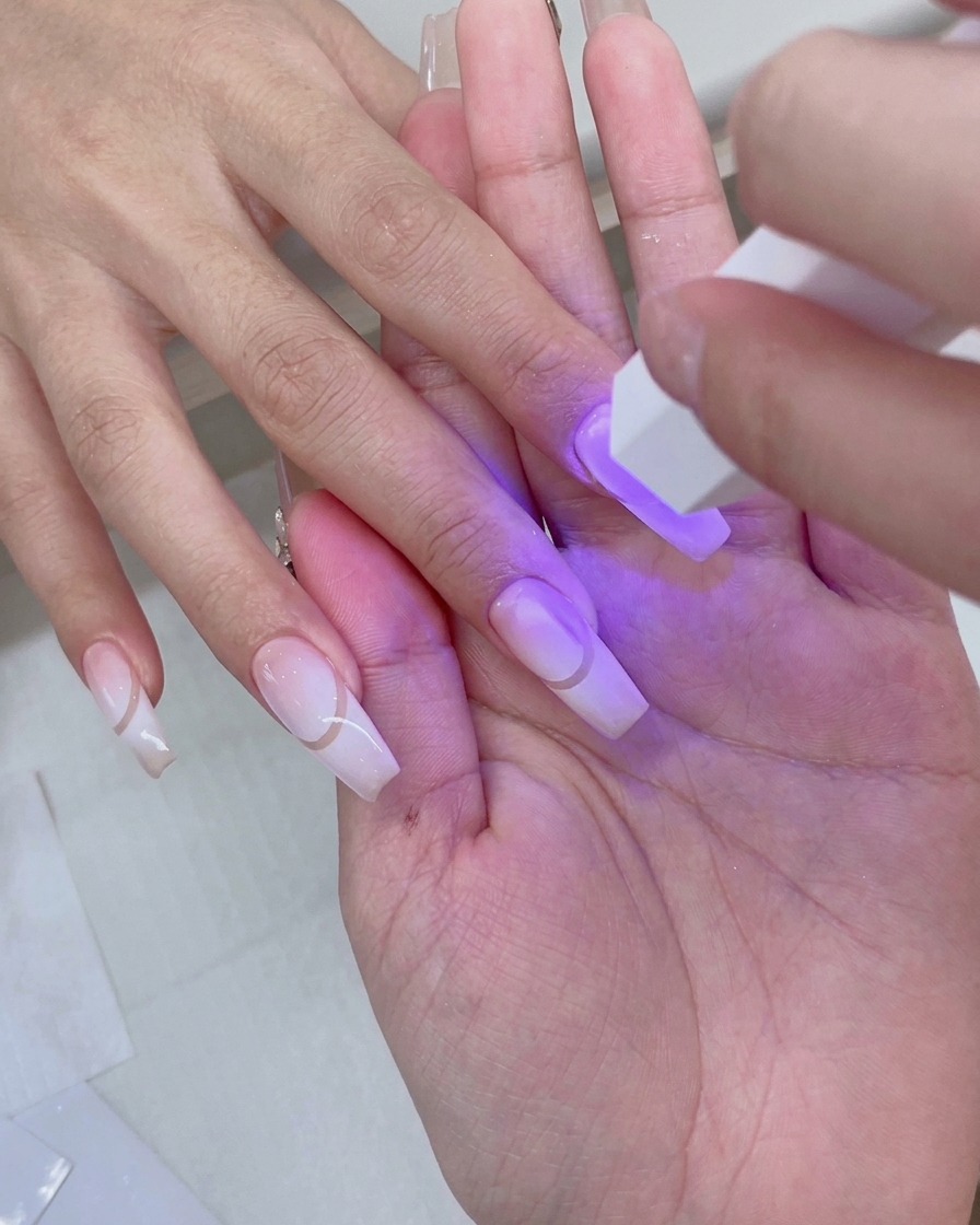 下準備されたグラデーションネイルを紫色の光が照らす、ピンクのUV/LEDネイルランプの中に手が置かれている様子。