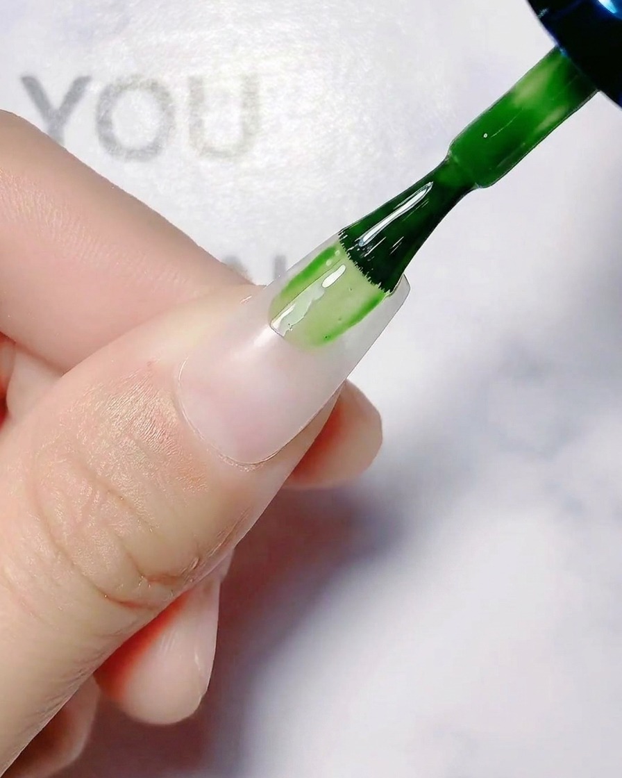 自爪に透け感のあるホワイトベースコートを塗っているネイルブラシ。