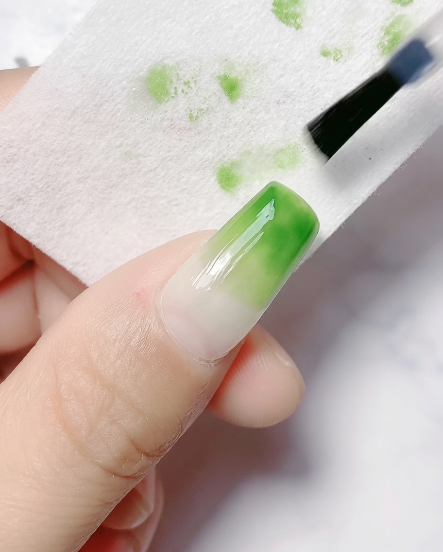 硬化したグラデーションネイルの未硬化ジェルをクレンザーパッドで拭き取っている様子。
