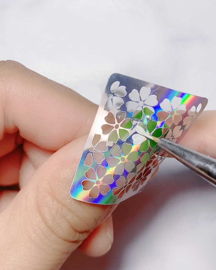 シールの中抜きされた花の形の中に、細筆でホワイトのカラージェルを塗っている様子。