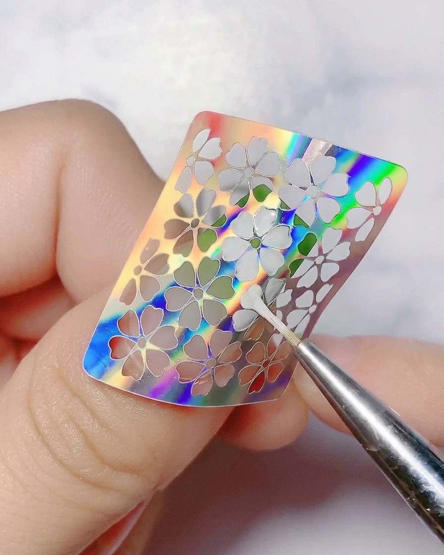 爪からホログラフィックフラワーシールを細い道具で剥がしている様子。