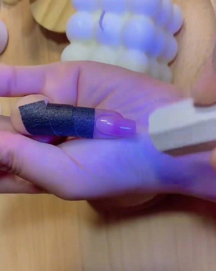 青い光が指と硬化されたグラデーションネイルを照らし出す、UV/LEDネイルランプの中に配置された手。