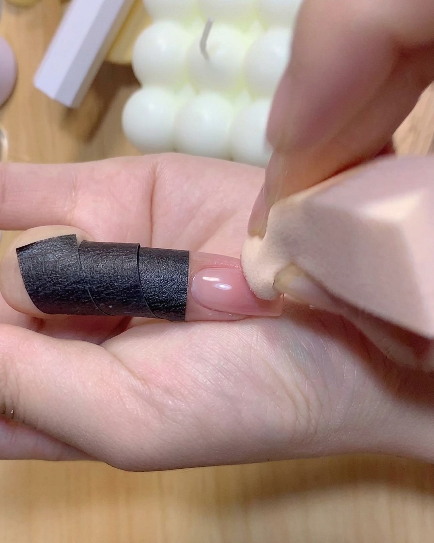 マニキュアを塗った爪にオンブレグラデーションを強めるため、ピンク色のカラーをスポンジでポンポンと乗せている様子。