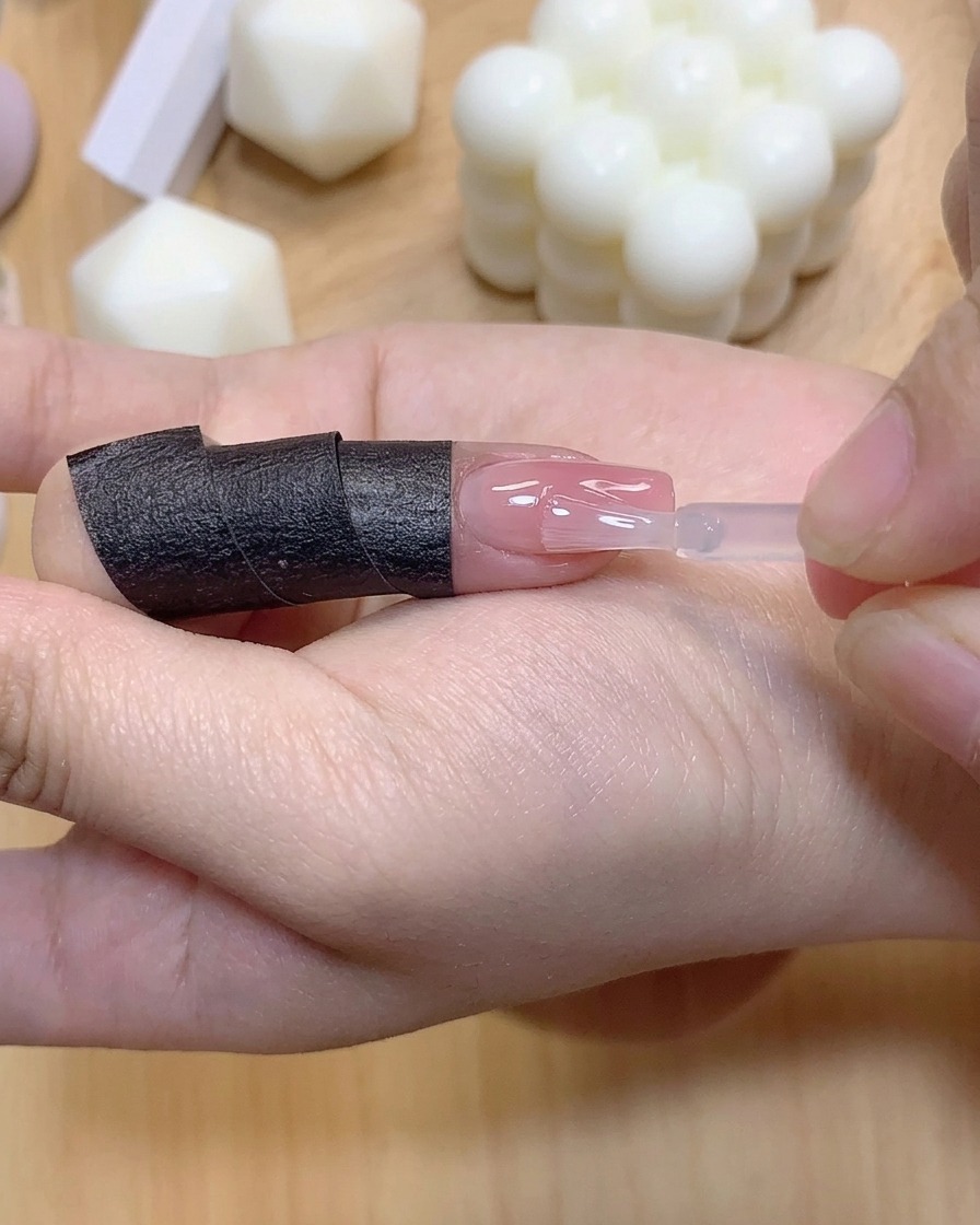 グラデーションカラーの爪の上にクリアな補強ジェルの層を小さなブラシで塗っている様子。