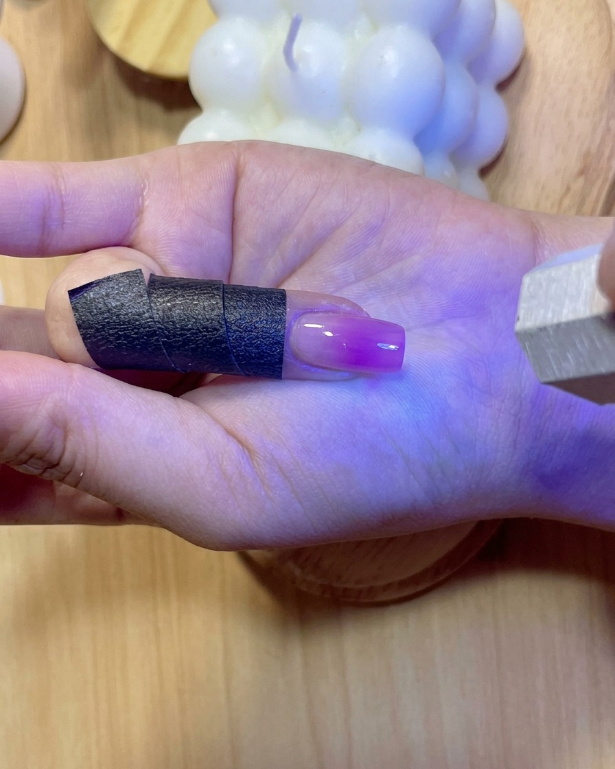 塗布された補強ジェルを硬化させながら、紫色のUV/LED光の下で輝く爪。