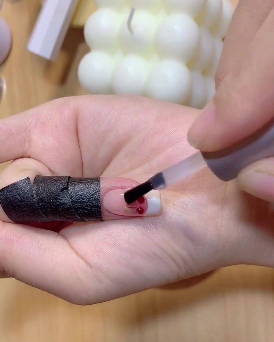 透明な3Dチェリーボールの上に半透明の赤色のジェルポリッシュをブラシで塗っている様子。