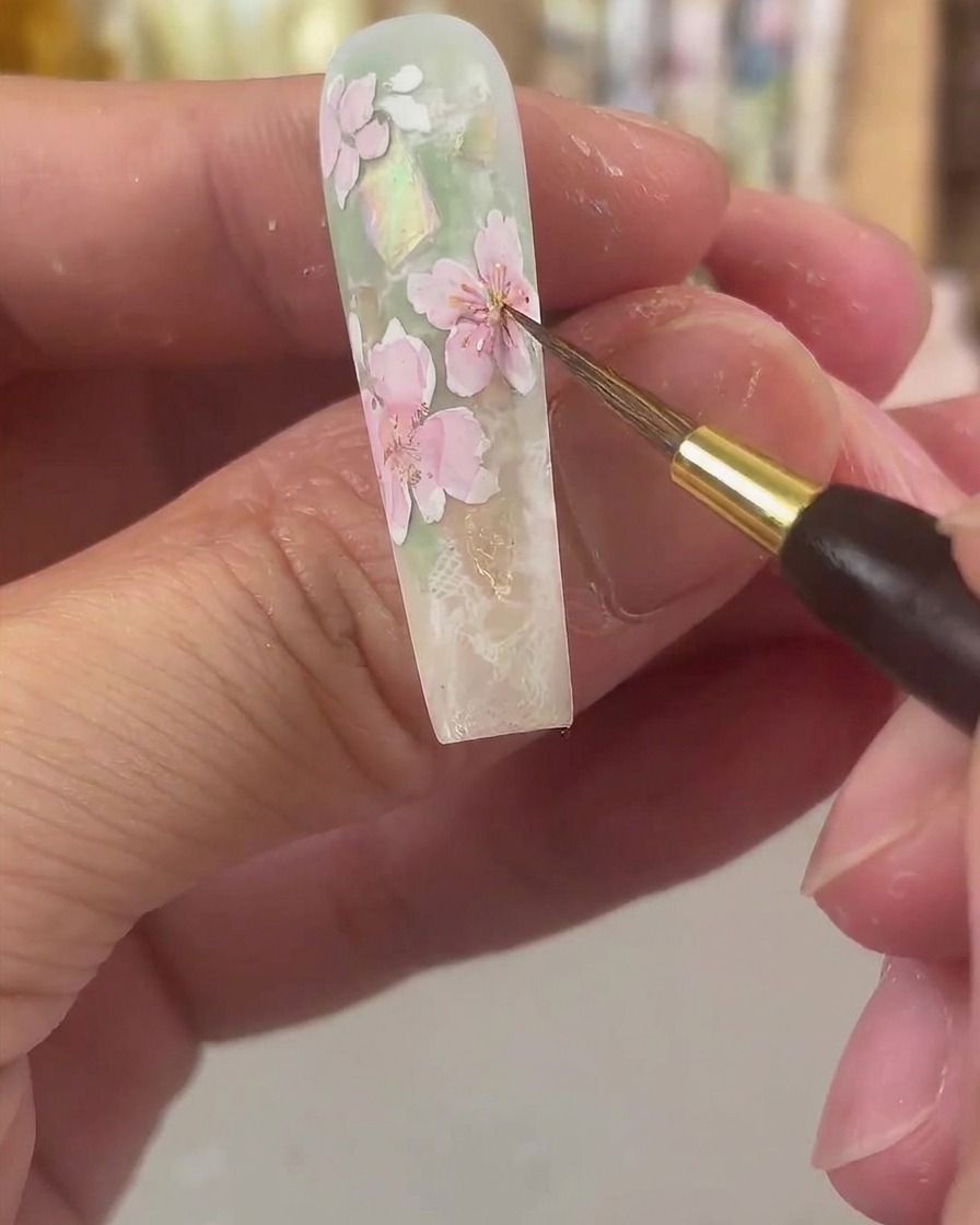 極細のディテールブラシで、ピンクに色づいた花びらの中心に鮮やかな黄色の水彩絵の具をポンポンとのせている様子。