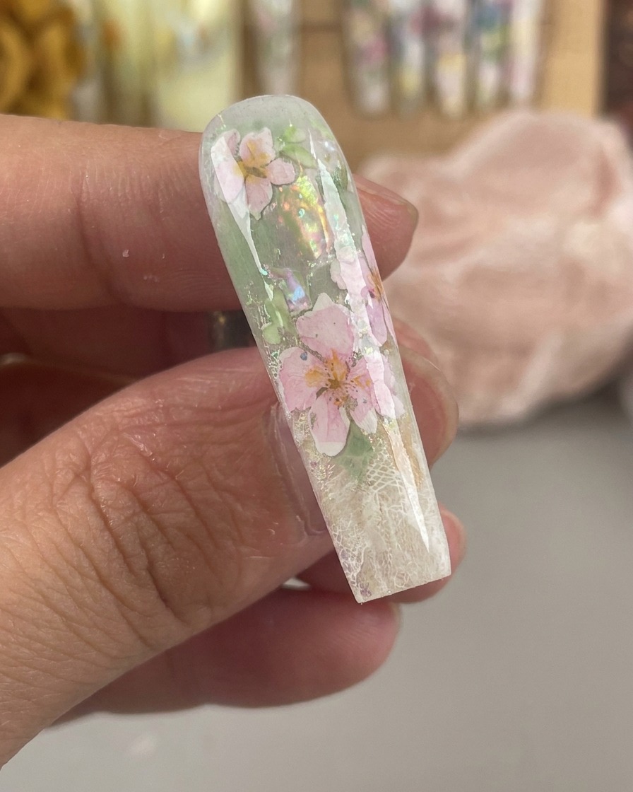 厚いクリアジェル層の下に、密封されたピンクと黄色の水彩の花が見える、ツヤのあるカプセル化されたネイル。