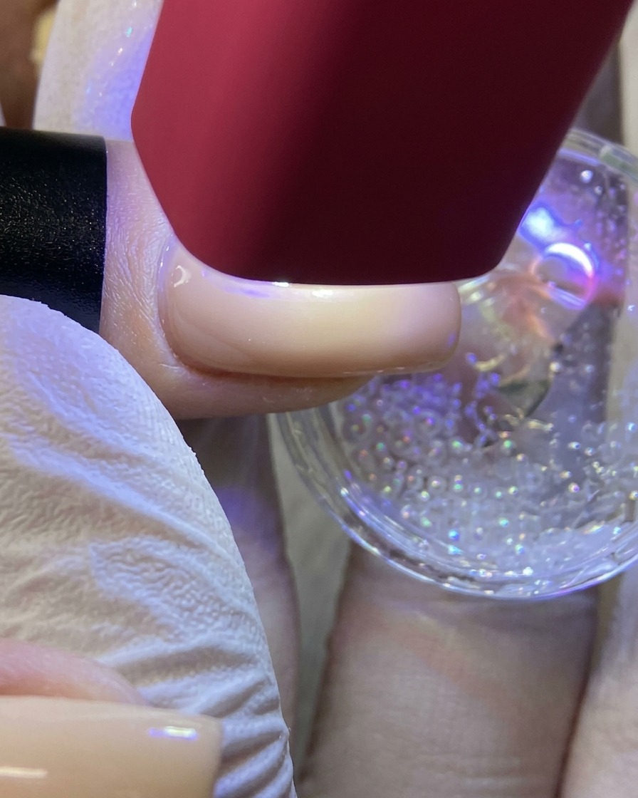赤いハンディUV/LEDライトで、グリッターでコーティングされた白い星のデザインを硬化している画像。