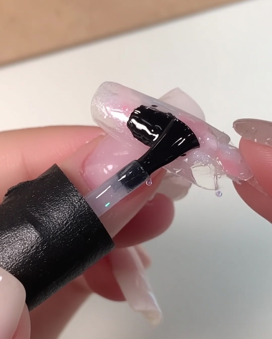ピンク、ホワイト、ブルーのマーブルネイルデザインの上に、黒いネイルブラシで厚めのクリアレベリングジェルを塗布している様子。