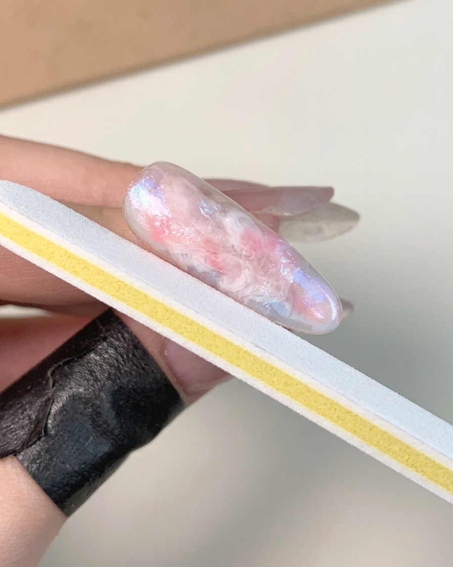 硬化してツヤが出たマーブルジェルネイルの表面を、白と黄色のネイルファイルストリップでバッフィングしている手元。