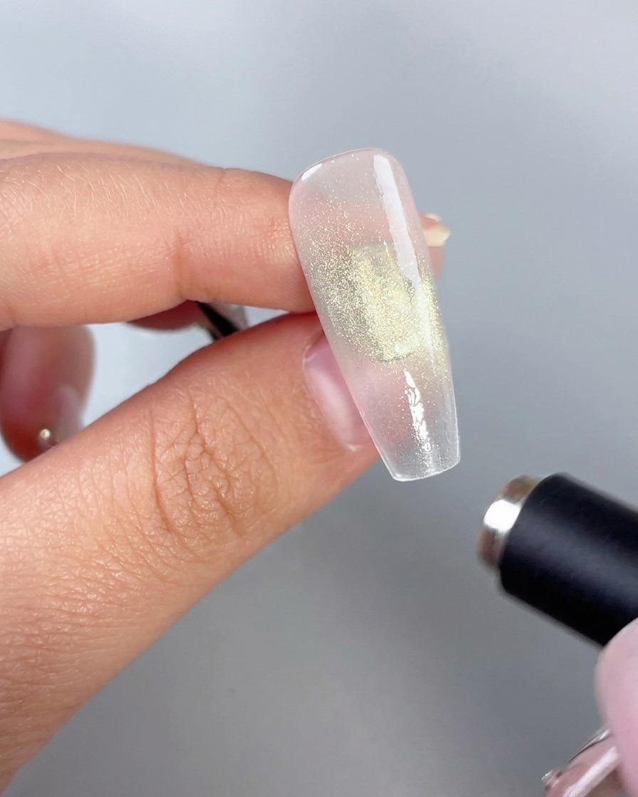 キャッツアイ効果を有効にするために、光沢のあるグリーンジェルネイルの近くに保持された円柱状のマグネットワンド。
