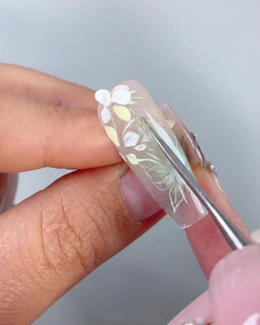 メタルツールが事前に成形された白い3D花びらをネイルのアドエスティブジェル上に配置している様子。