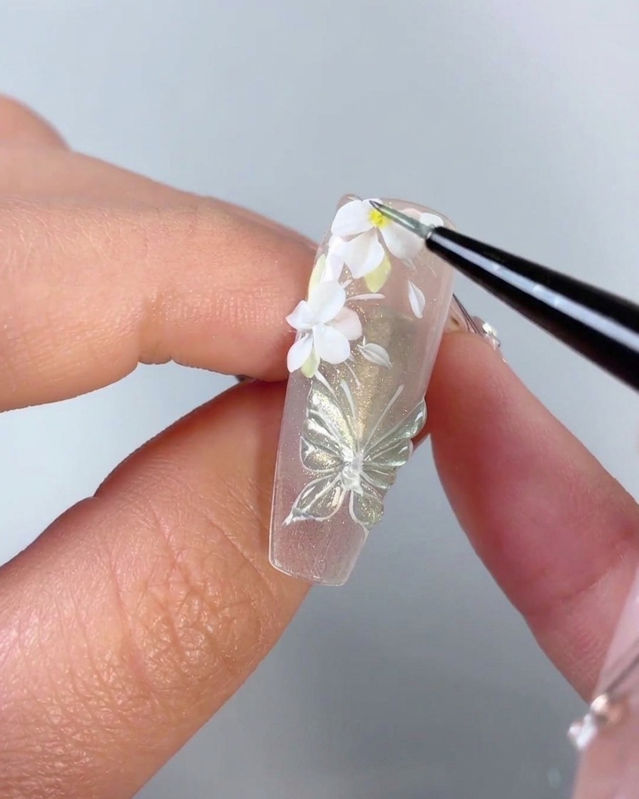 ネイル上の白い3Dフラワーの中心に、細かいブラシが小さな黄色のドットを追加している様子。
