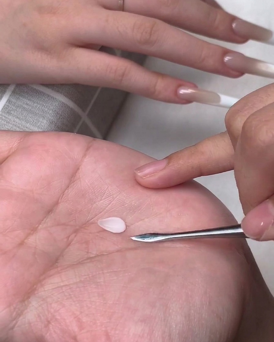 金属製カービングツールの隣にある人の手のひらに置かれた、小さなしずく型の白い3Dジェルの花びら。