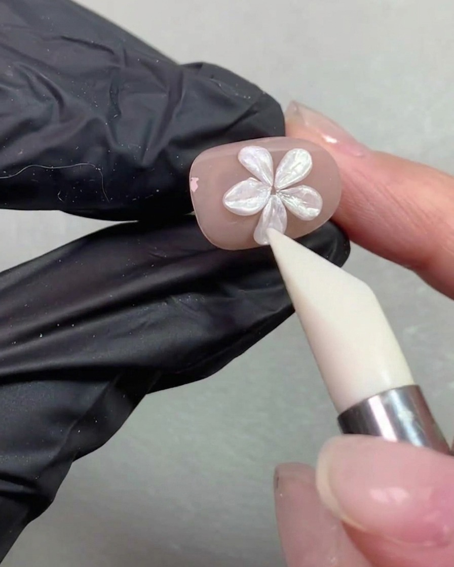 シリコンシェーピングペンがヌードカラーの爪の上にあるパールフラワーの花びらの形を滑らかに整えている様子。