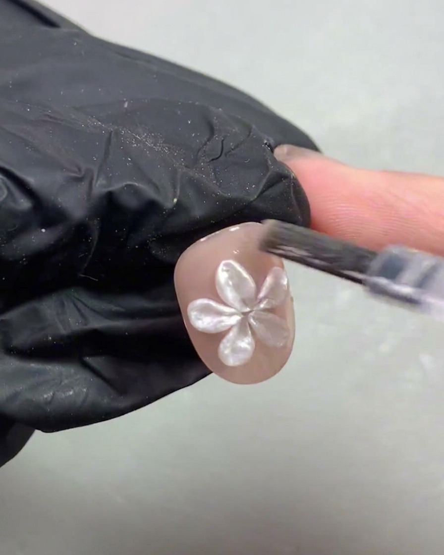 3Dホワイトパールフラワーで飾られた短い爪を、手袋をつけた手が紫色のUV/LED硬化ランプに入れている様子。
