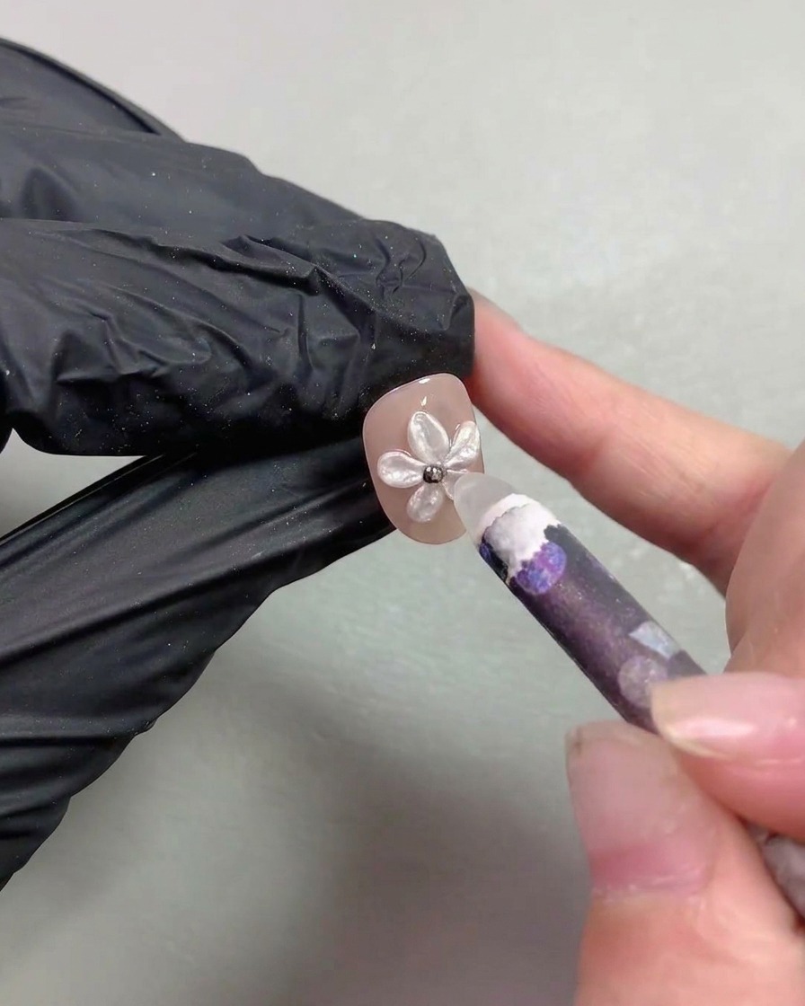 ワックスピッカーツールが、パールフラワーネイルの中央に小さなメタリックのスティールビーズを配置している様子。