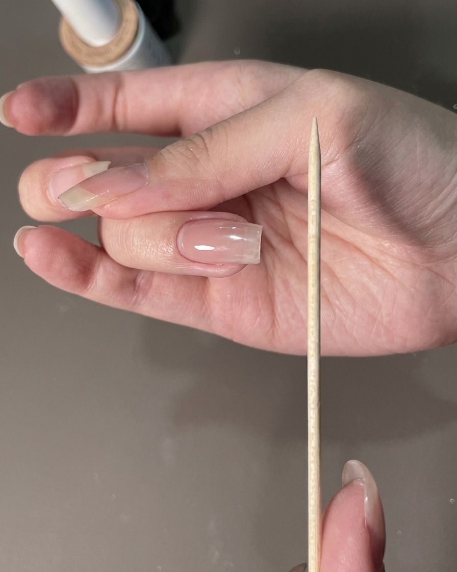 マニキュアを施した手のそばで、爪のエッジを整えるために持たれているネイルファイル。