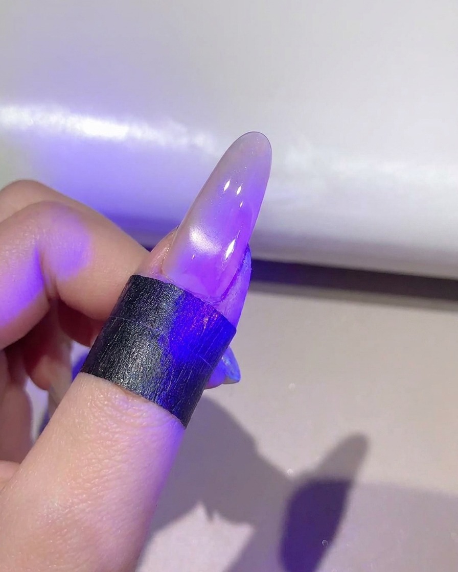 紫色のUV/LEDランプの下で、完成したキャッツアイジェル層を硬化させている爪。