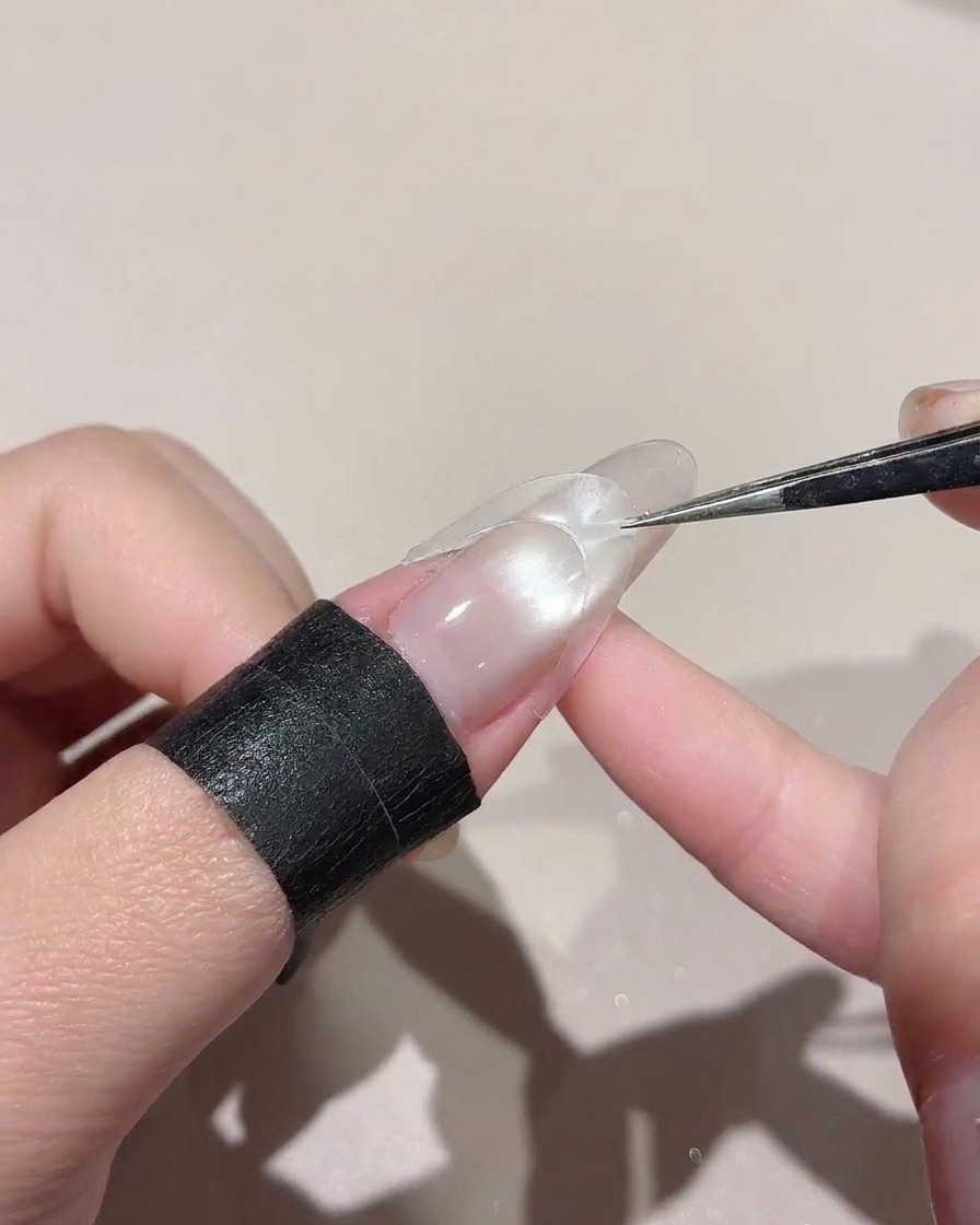 ピンセットを使い、光沢のある爪の中央にカーブしたステッカーを配置している様子。