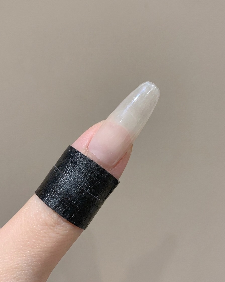 白い角度のついたシリコンツールを使って、指に貼られたフレンチネイルステッカーのカーブしたエッジを押し下げている様子。