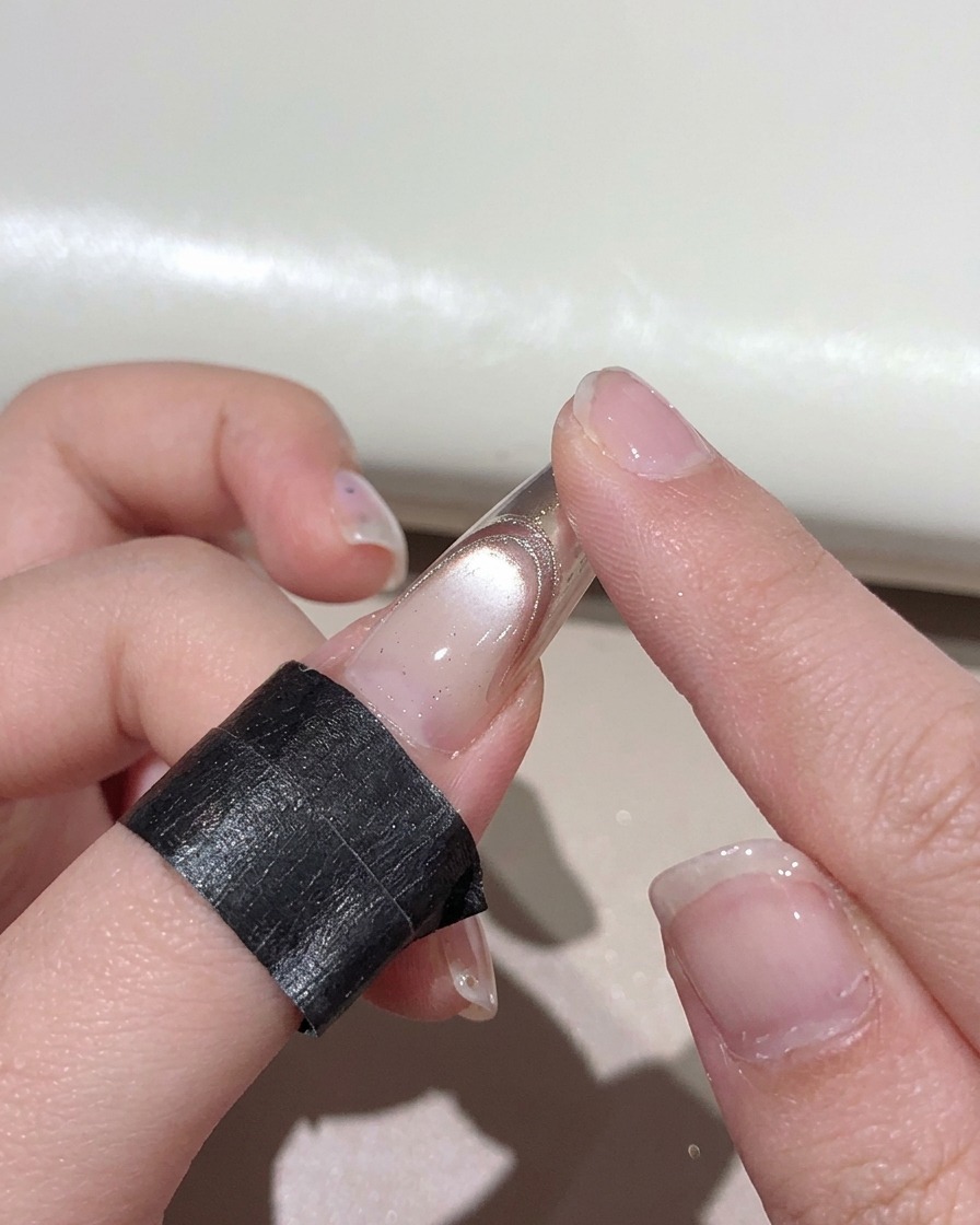 マニキュアが施された爪の先端に、素指を使ってローズゴールドのメタリックパウダーを擦り込んでいる様子。