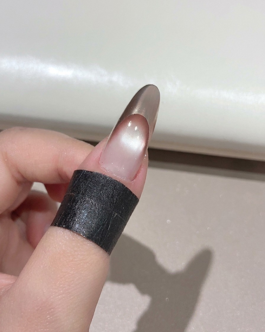 完成したゴールドローズのフレンチマニキュアの上に、ネイルブラシでクリアな艶出しトップコートを塗布している様子。