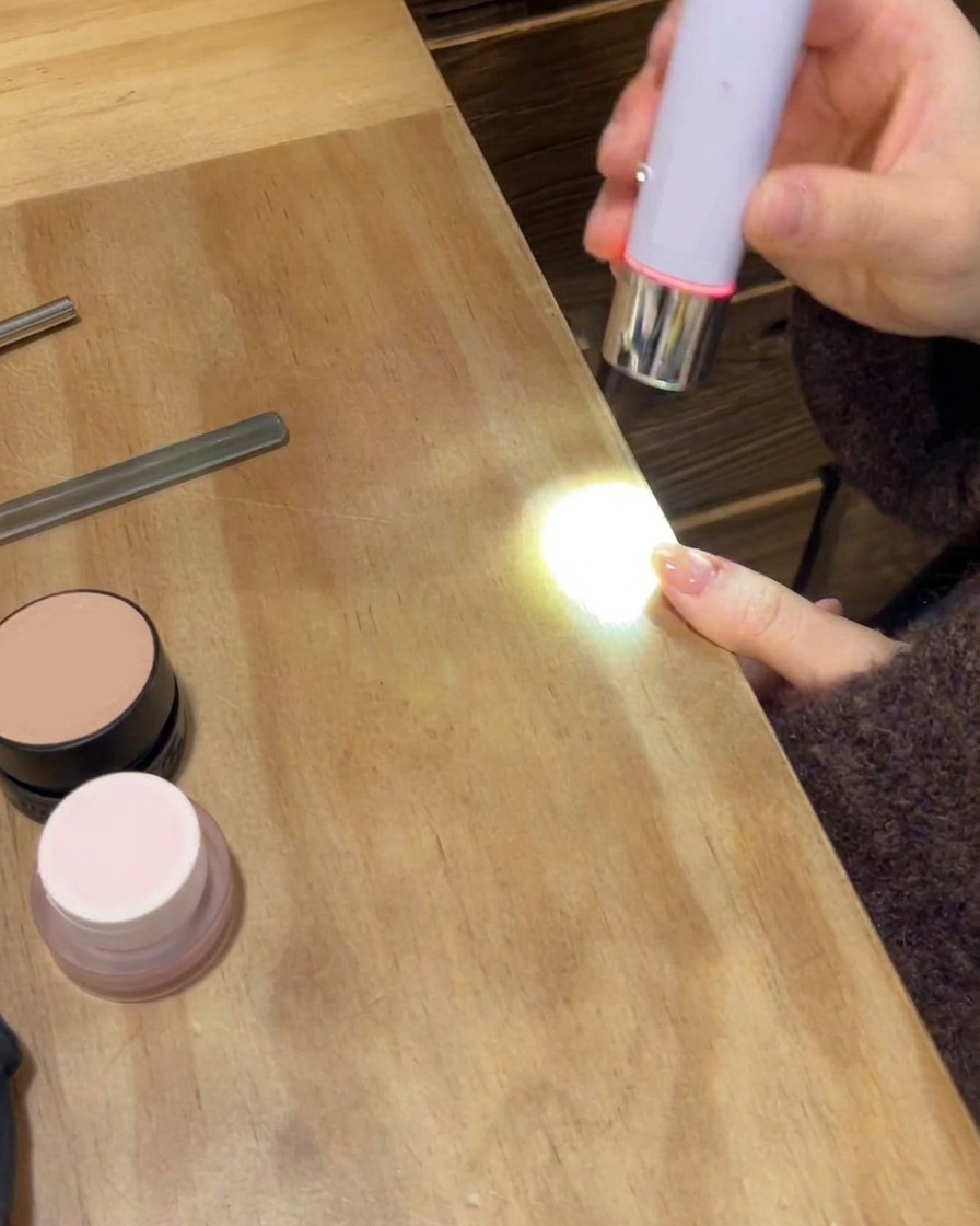 ポータブルUV/LEDランプがマニキュアを施した手の最終的なツヤのあるトップコートを硬化させている様子。