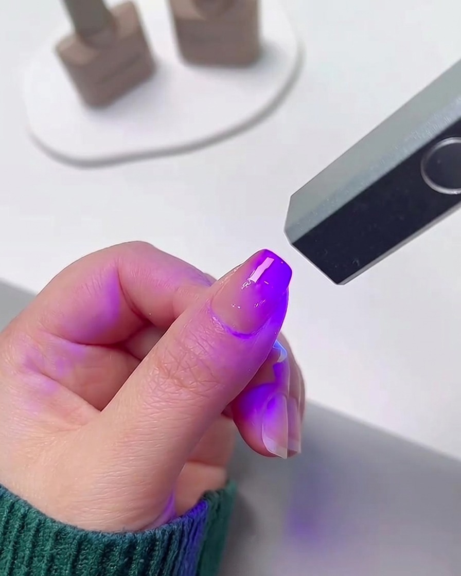 ジェルポリッシュを硬化させるため、明るい紫色の光を放つ小型のポータブルUV/LEDネイルランプの下に置かれた指。