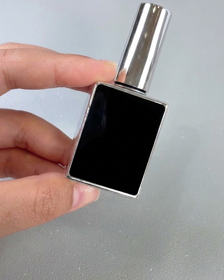 ニュートラルな背景を背に、手で保持されているスクエア型の黒と銀のネイルトップコートボトル。