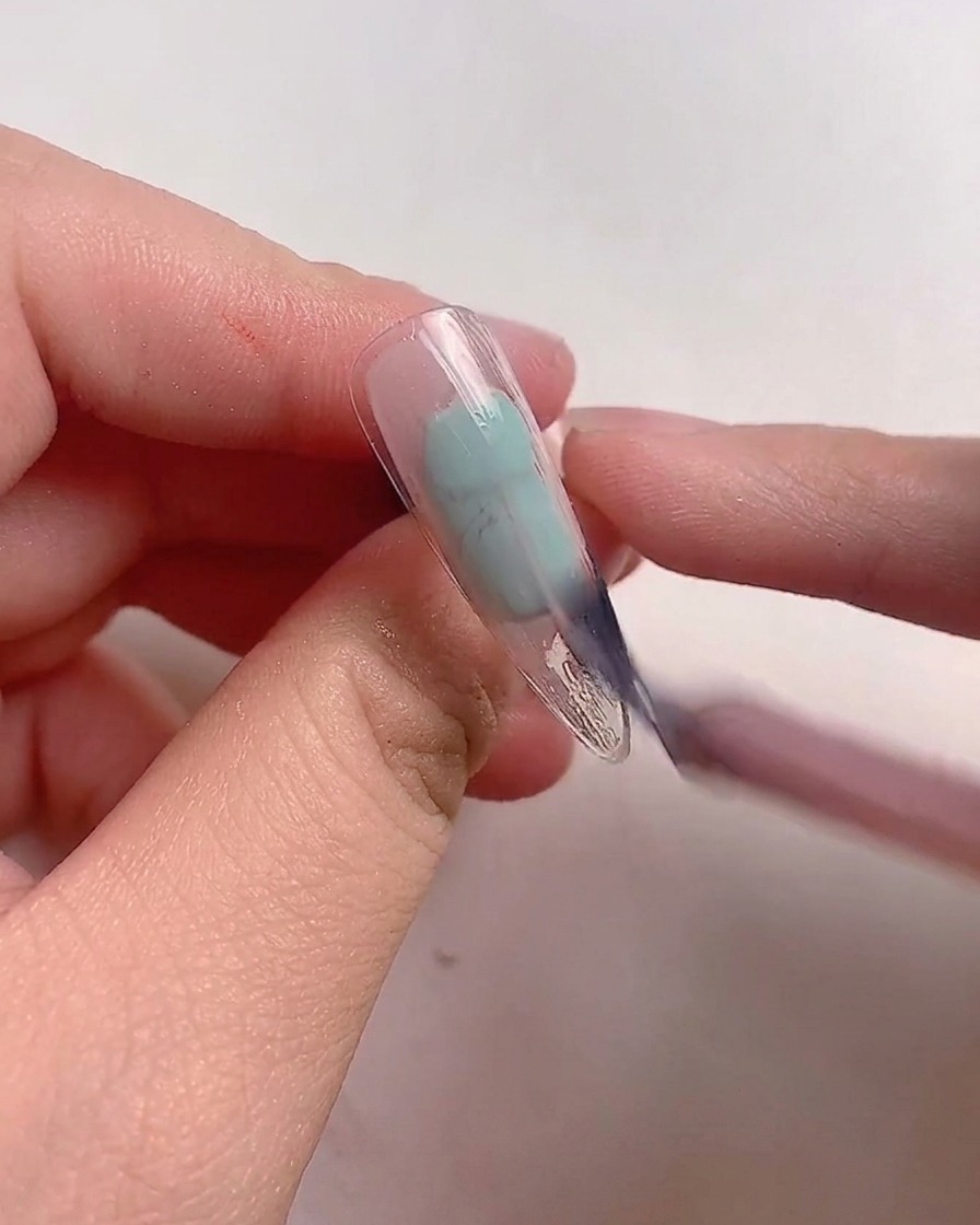クリアネイルチップにモーブピンクのジェルポリッシュをブラシで塗る様子。