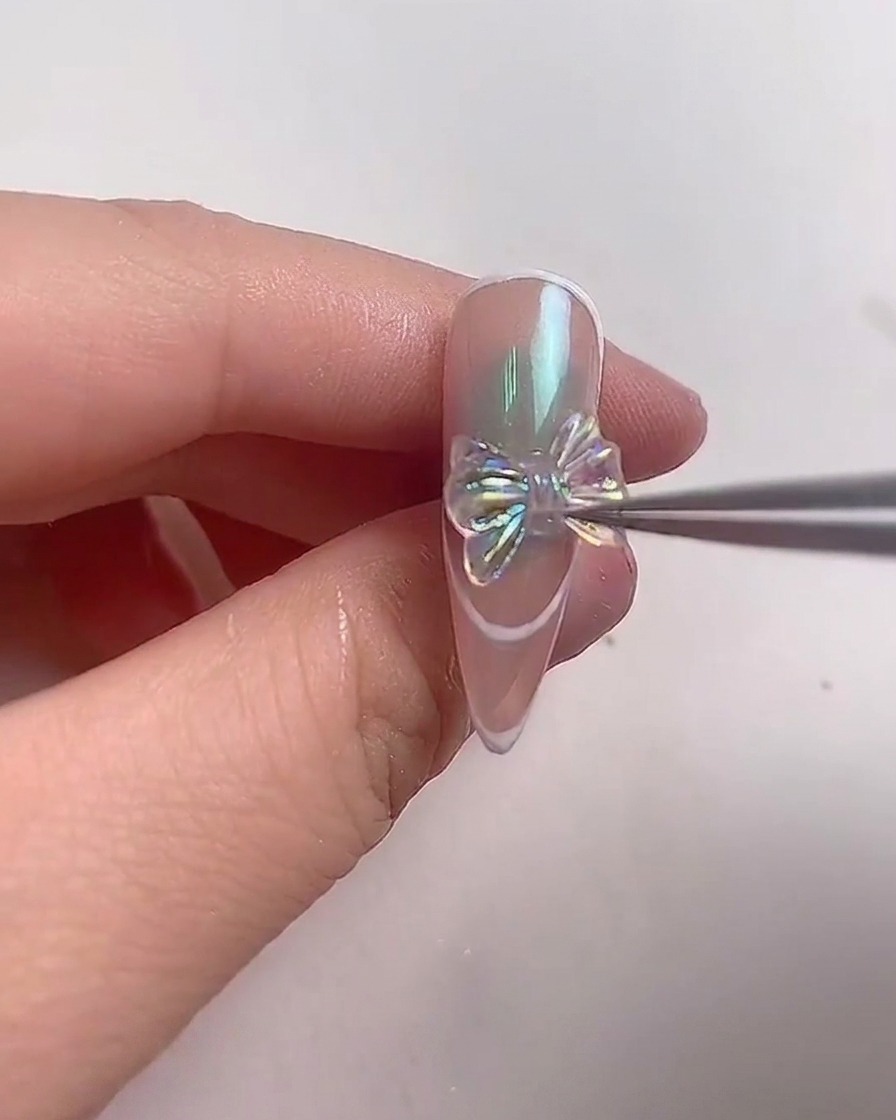 金属製のピンセットを使用して、アーモンドシェイプのネイルの中央に輝く偏光クリスタルリボンを慎重に配置する様子。