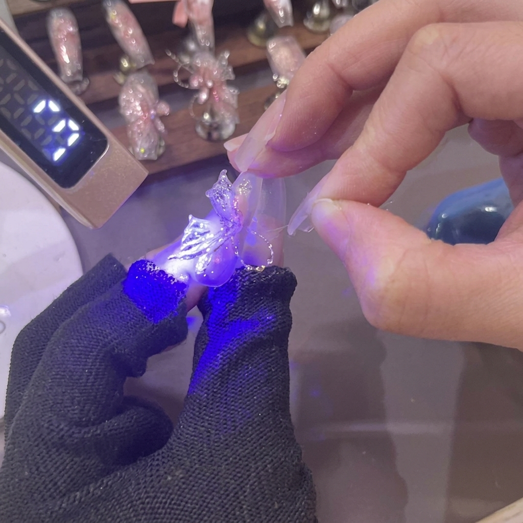 爪の上の新しく成形された3Dピンクジェルバタフライウィングに、ミニUVランプが紫色の光を照射している様子。