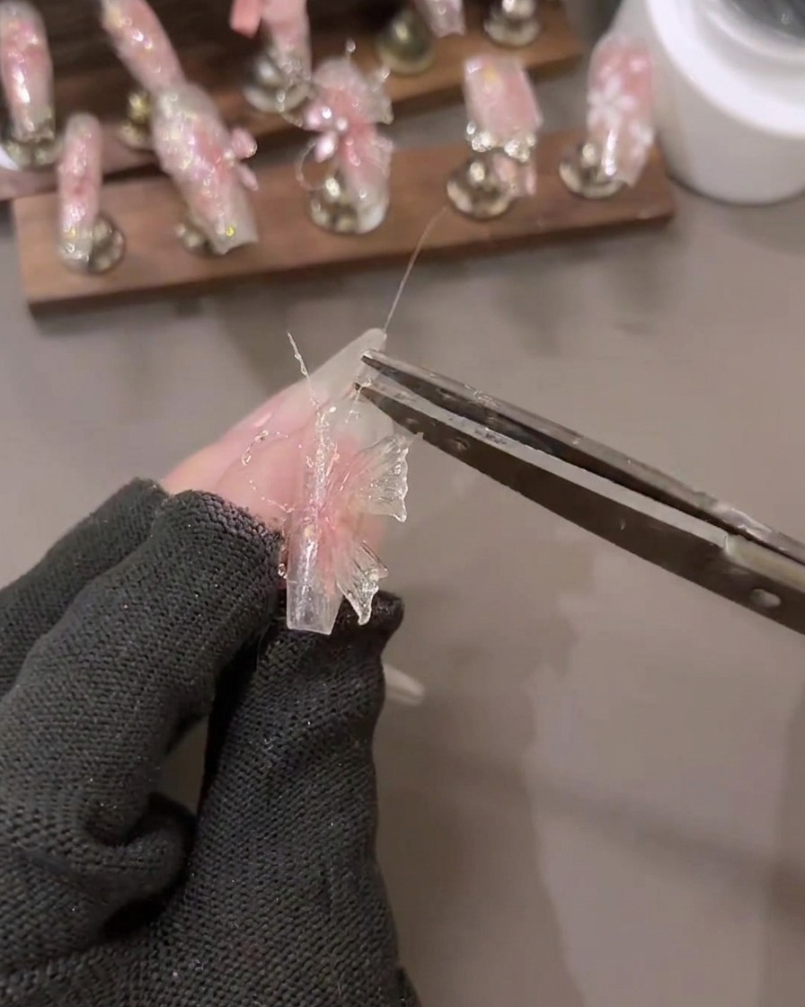 近くにツールが置かれた3Dネイルアートデザインに、シャッタードダイヤモンドグリッタージェルの詳細を適用している手のクローズアップ。