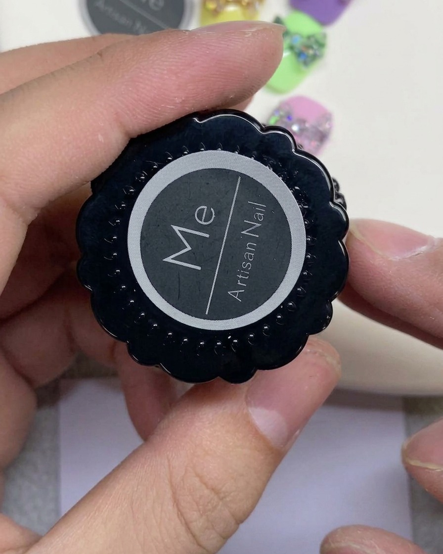 白い丸型ロゴが入った黒いアルチザンネイルのジャーを片手で持っている様子。