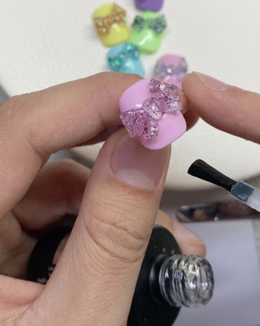 塗装されたピンクのネイル上の3Dグリッターリボンの周りに、ネイルブラシでクリアトップコートを塗布しているクローズアップ。